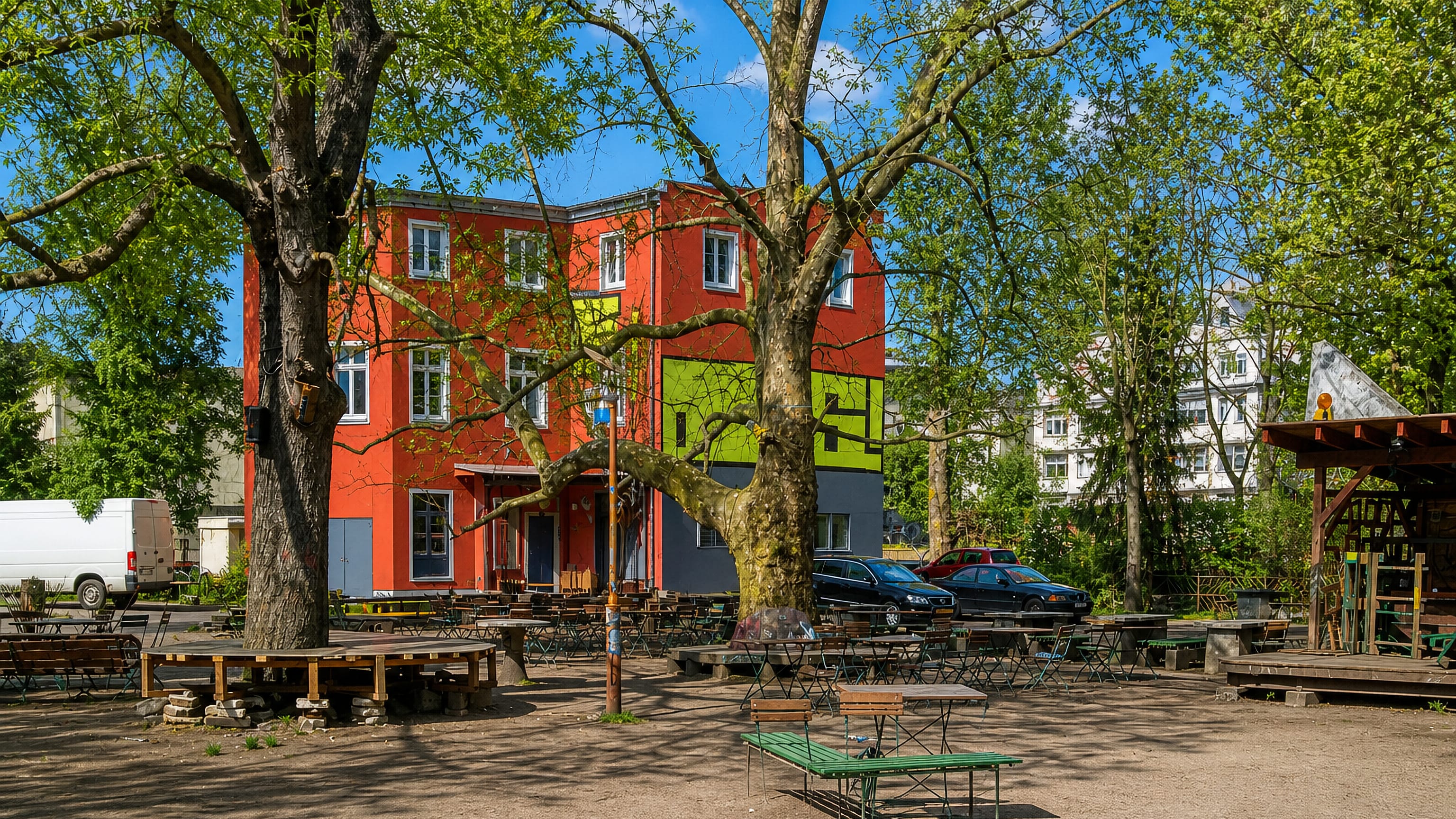 Shaded beer-garden courtyard with benches beside a brightly painted corner building in Connewitz, Leipzig.