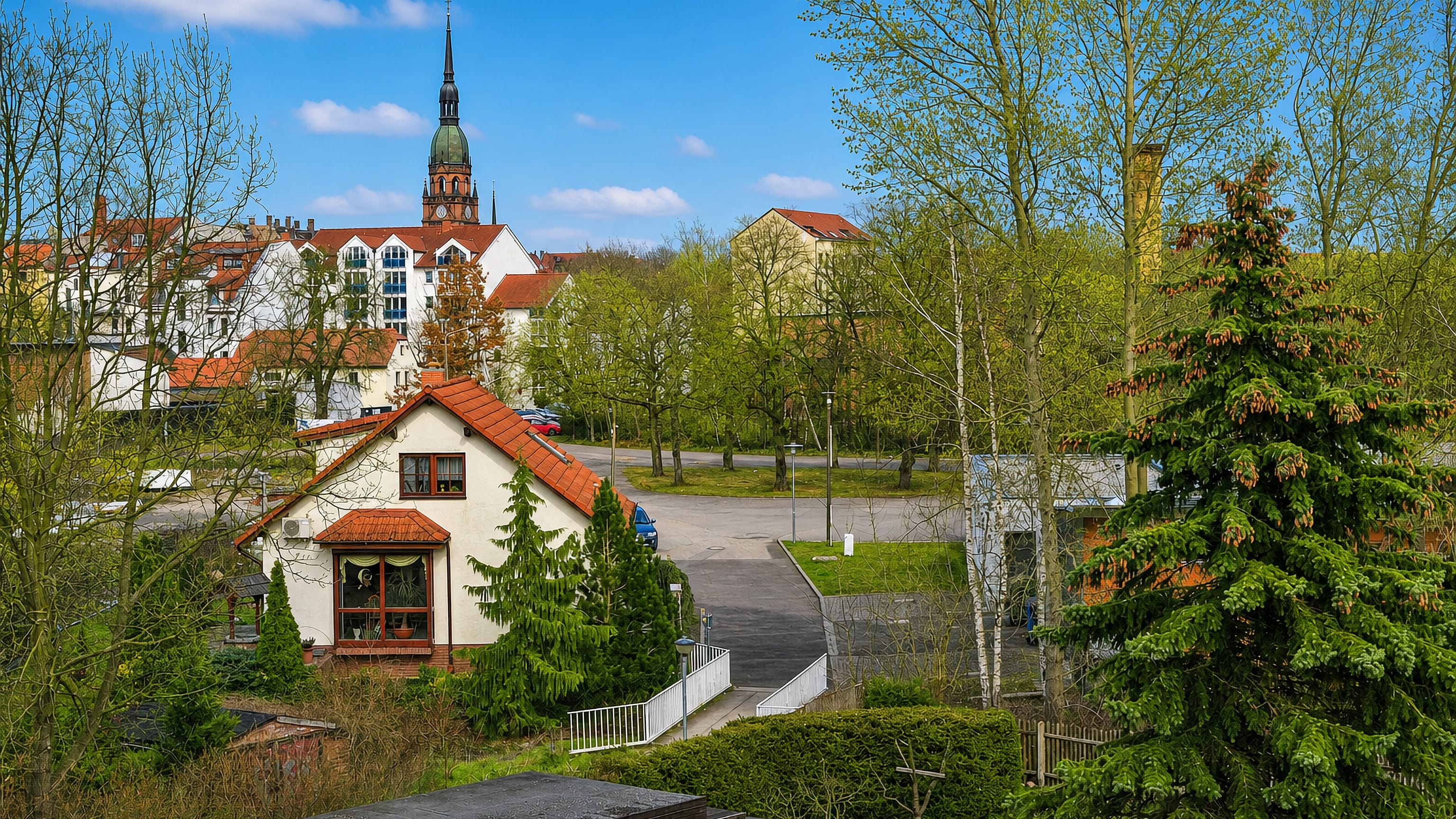 Suburban houses with red-tiled roofs below a green-spired church tower in Sellerhausen, eastern Leipzig, Germany.
