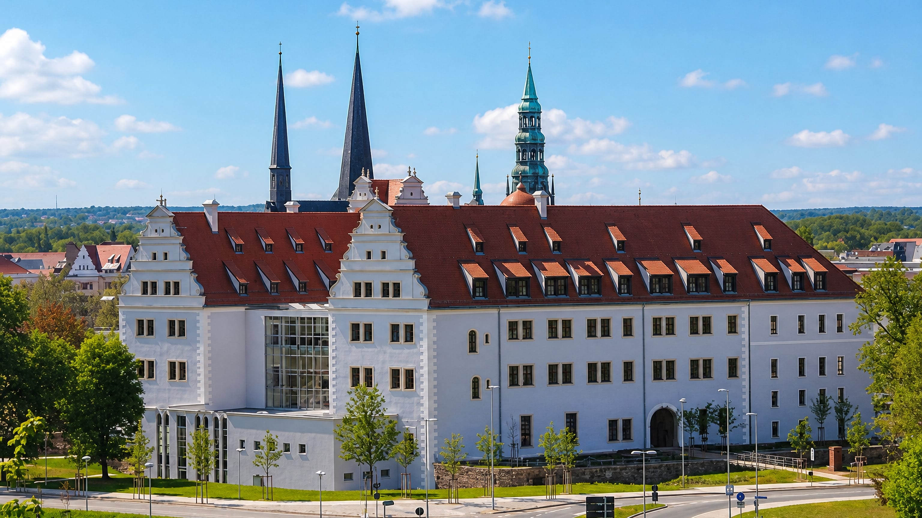 Schloss Osterstein's white gabled facade in Zwickau with the city's church spires and green tower behind.