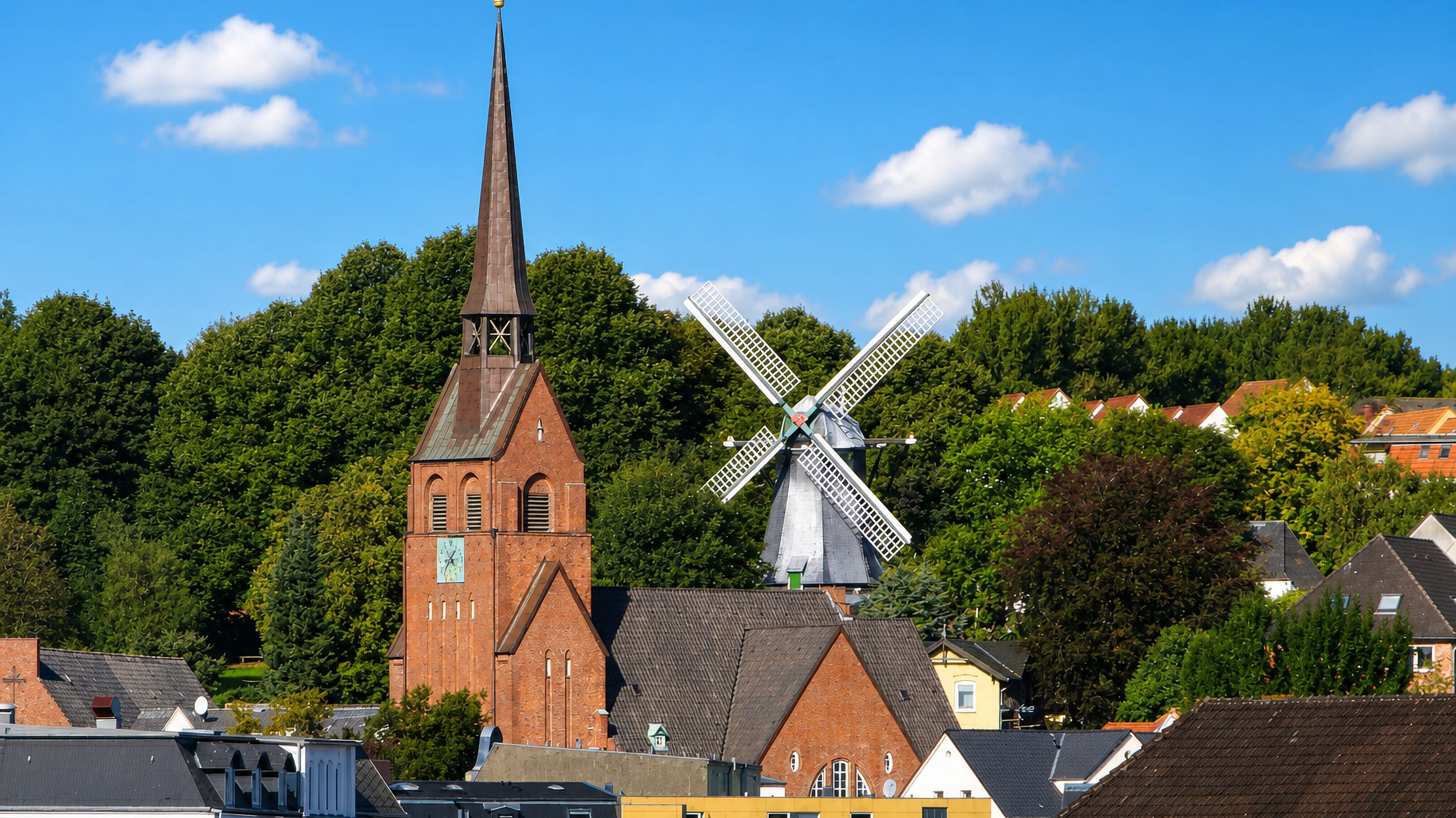 Brick church spire and a white-sailed windmill rising above the rooftops of Nordstadt, Flensburg.