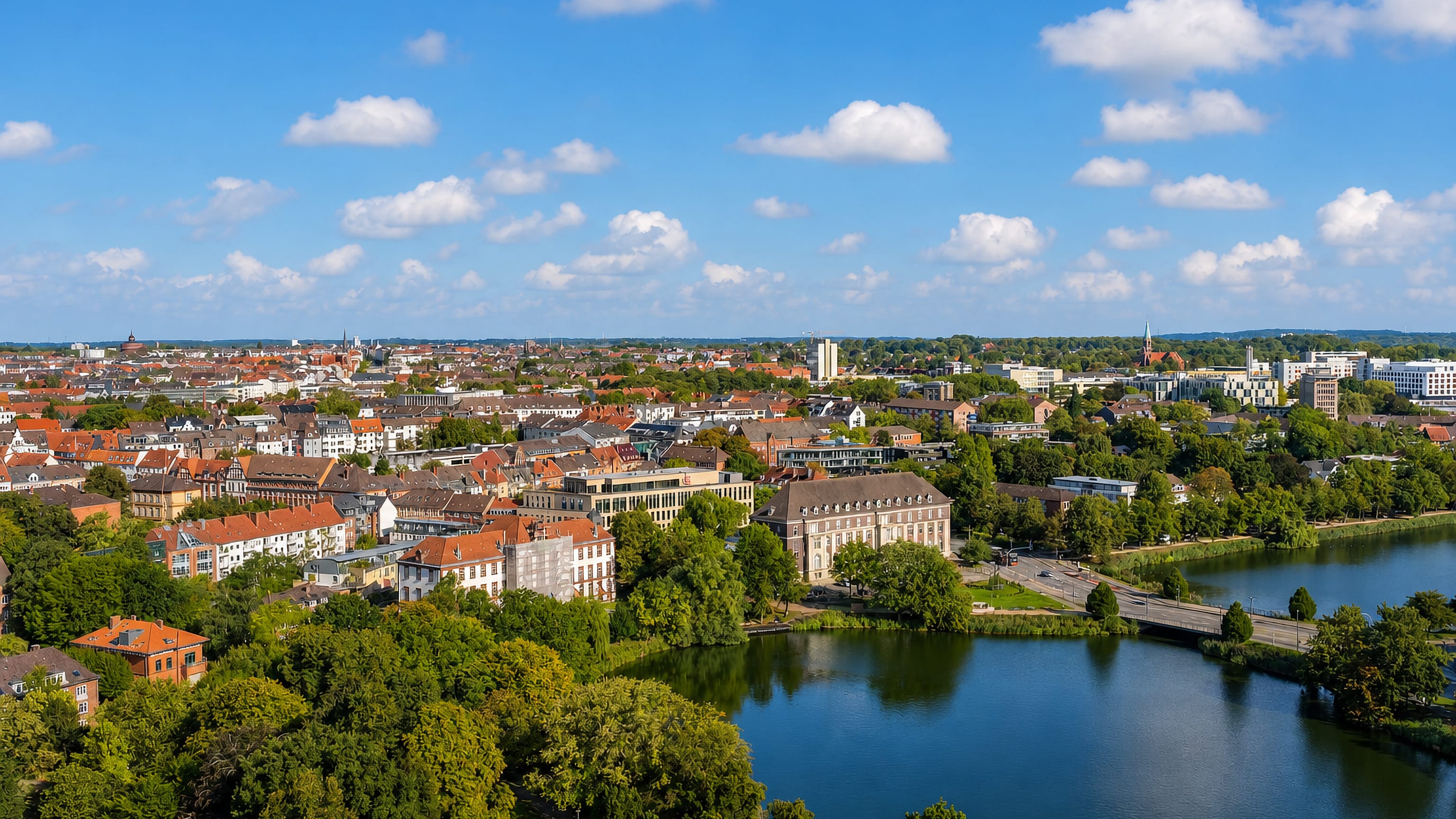Aerial view across Damperhof in Kiel, with a park-fringed lake and the city's rooftops beyond.