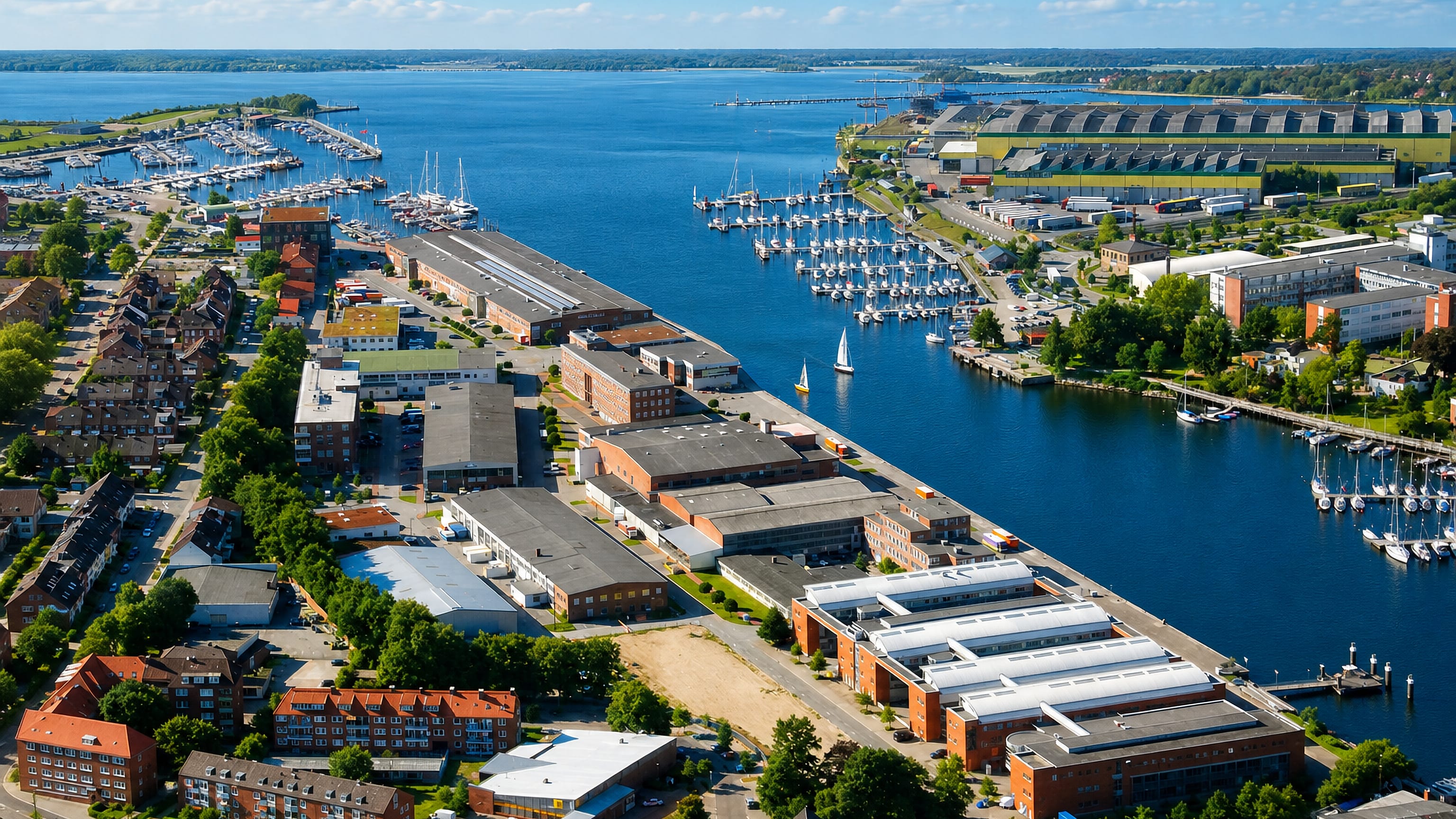 Aerial view of Neumühlen-Dietrichsdorf in Kiel, with marinas, shipyard sheds and brick housing along the fjord.