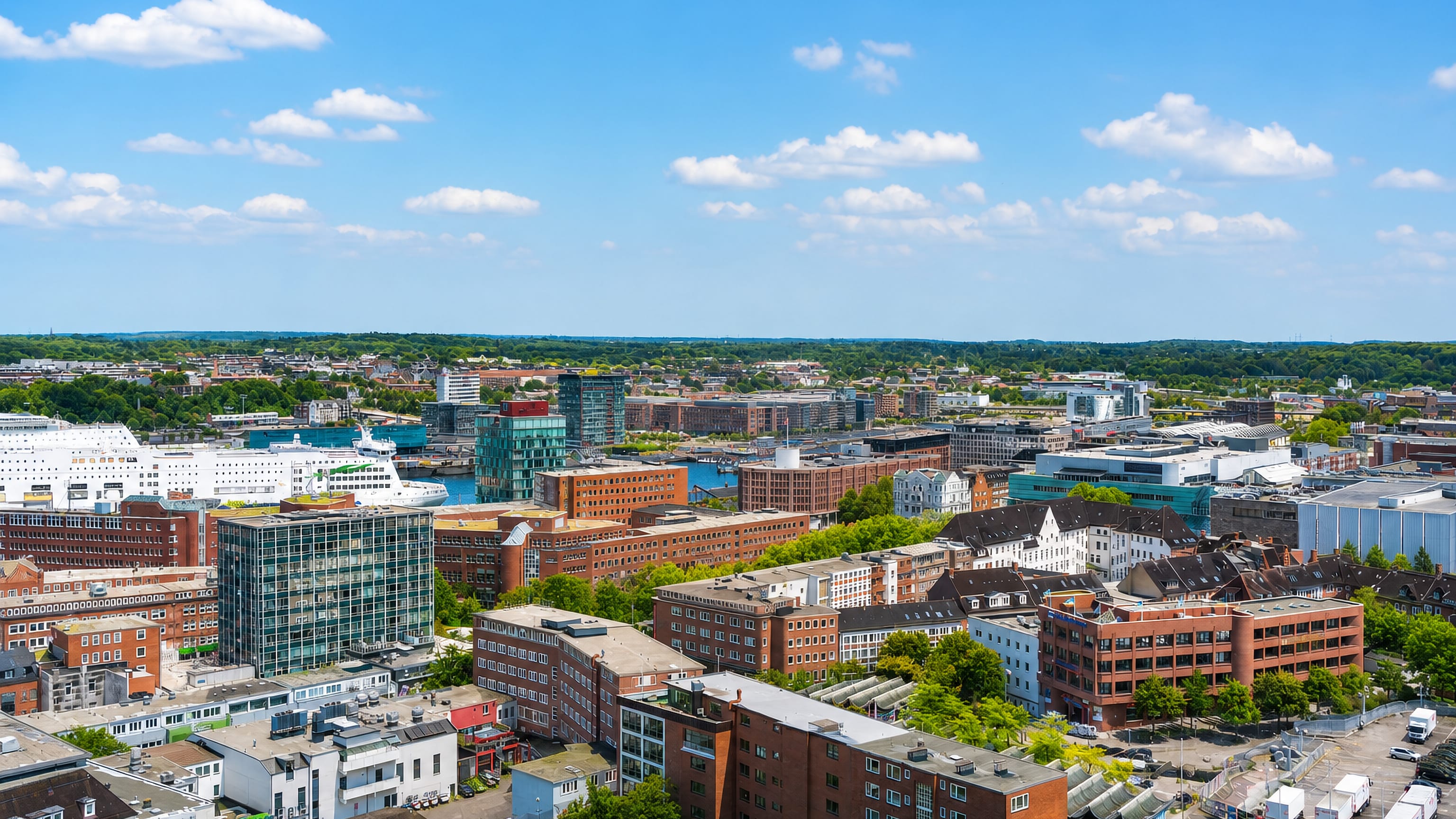Aerial view over Vorstadt in Kiel, with red-brick blocks, glass offices and ferries moored on the Kiel Fjord beyond.