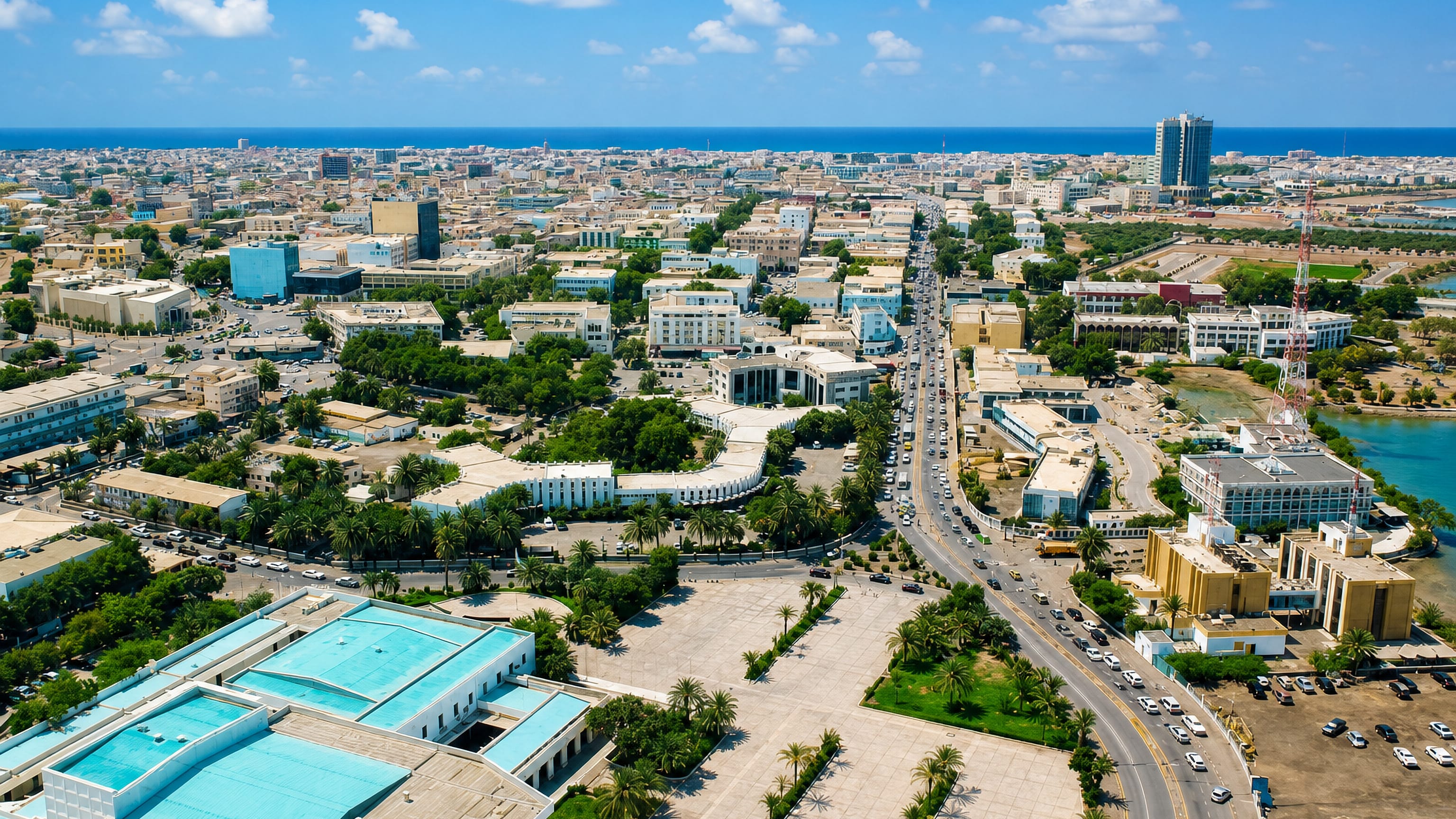 Aerial view over Djibouti City's low-rise streets and palm-lined plaza with the Gulf of Tadjoura beyond.