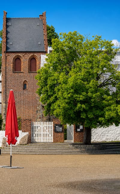 Ballerup town square in Denmark with a medieval brick church tower, a fountain and outdoor cafe parasols.