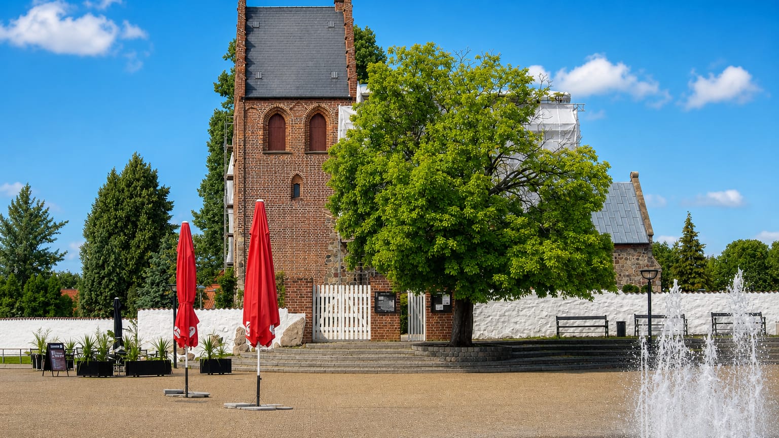 Ballerup town square in Denmark with a medieval brick church tower, a fountain and outdoor cafe parasols.