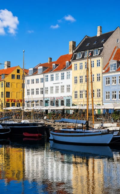 Nyhavn's colorful waterfront townhouses and moored wooden boats reflected in the canal in Indre By, Copenhagen, Denmark