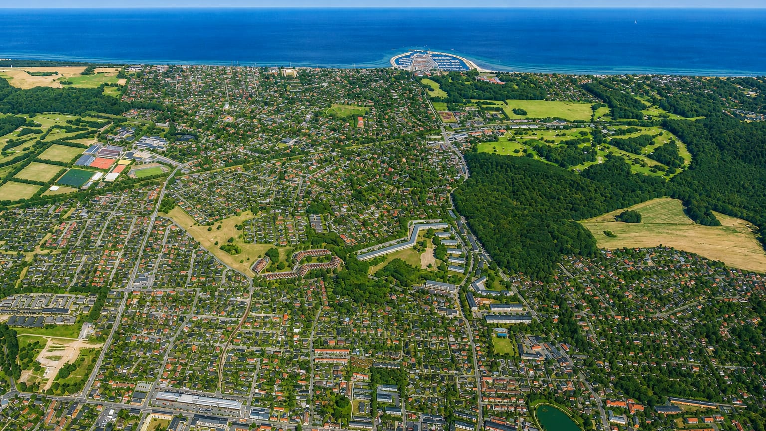 High aerial of Hørsholm's green suburban streets reaching a marina on the Øresund coast