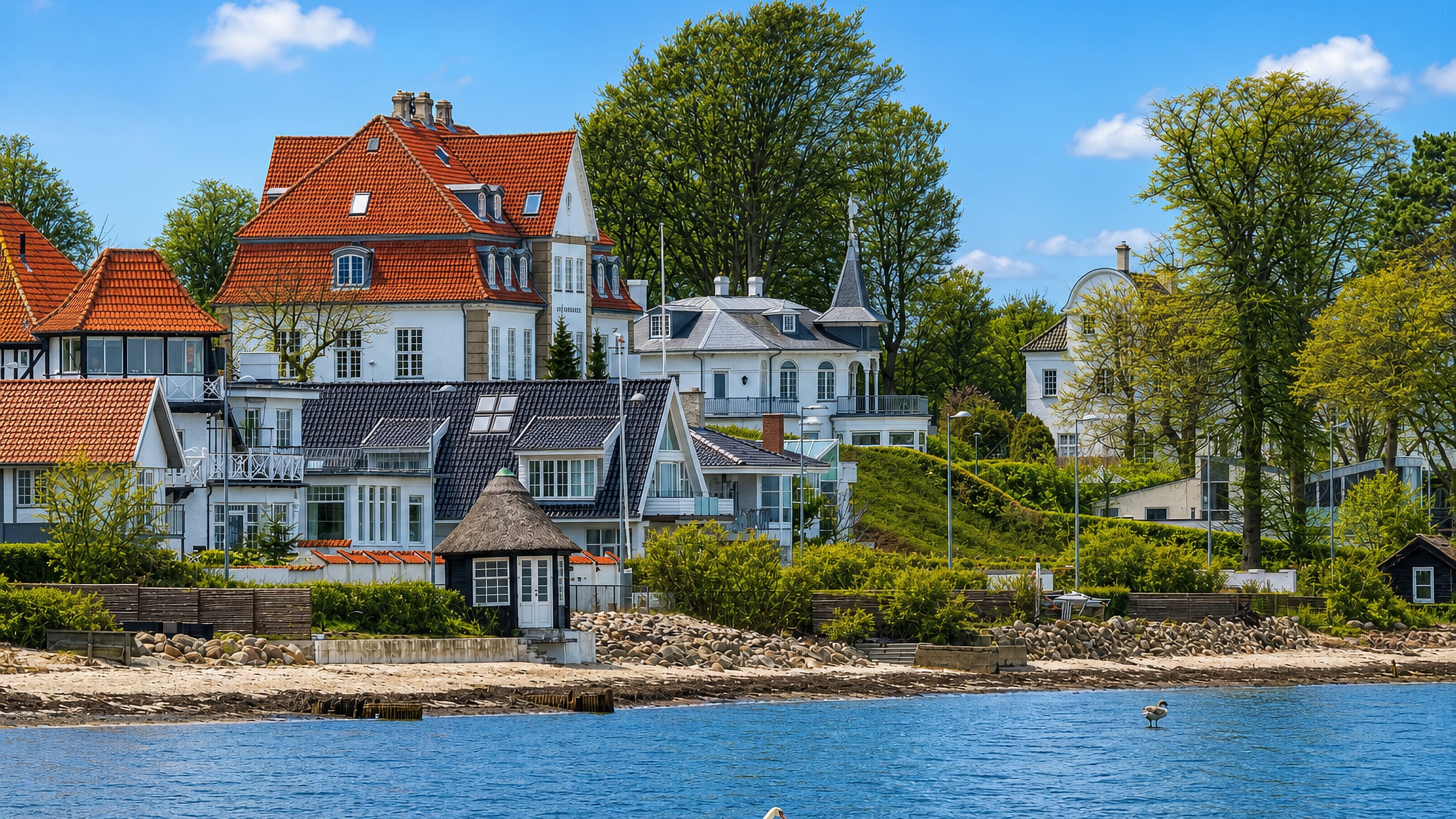 Waterfront villas with red-tiled roofs above a stony beach on the Oresund shore at Rungsted Kyst, Denmark