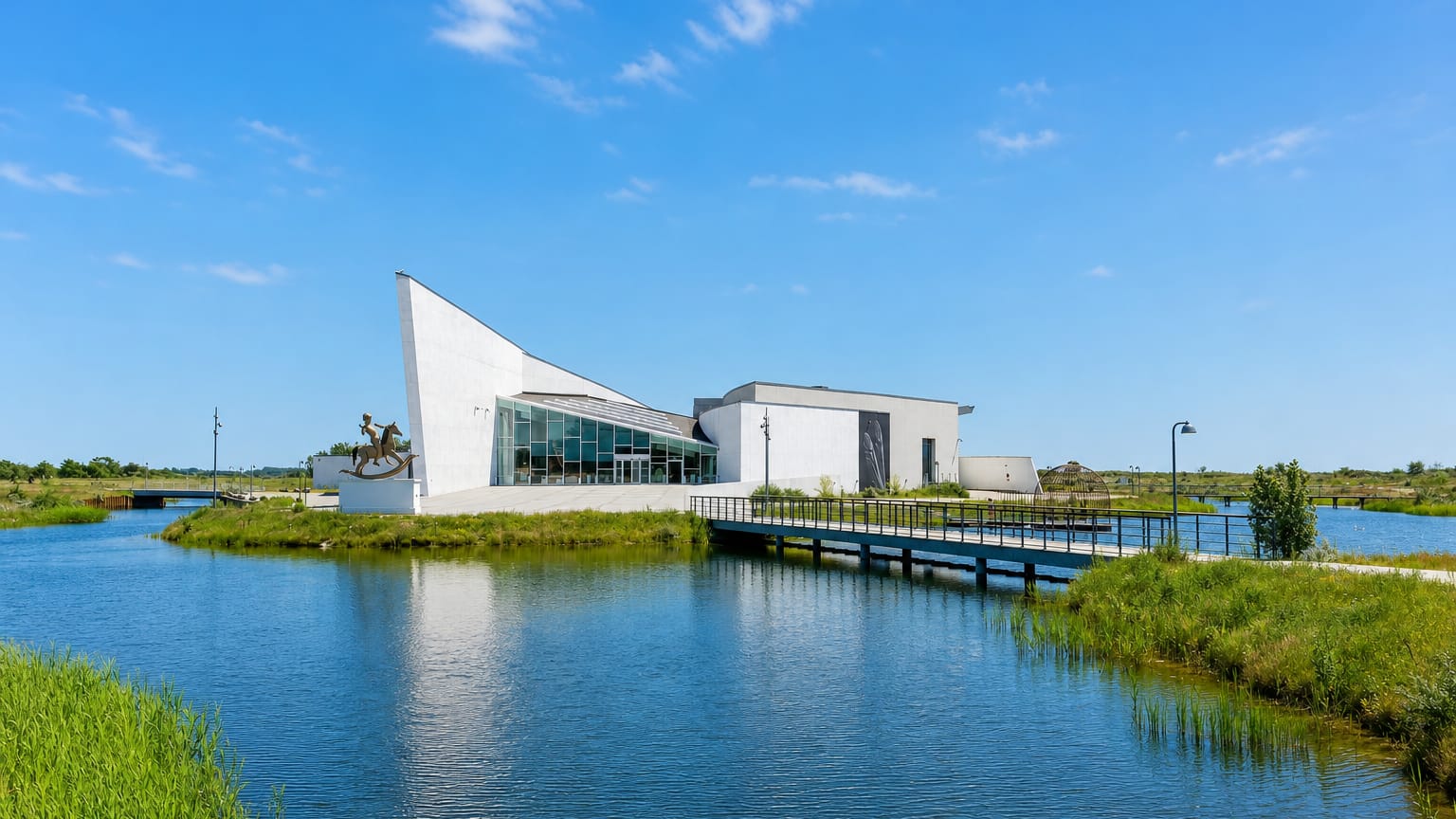 Ishøj's white Arken museum building with an equestrian sculpture and footbridge over a reed-fringed lake.
