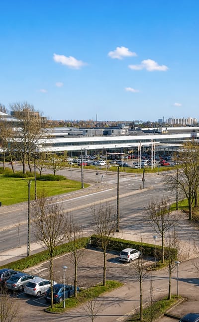 Daytime view over Rødovre, Denmark: low-rise commercial buildings, tree-lined roads and green parkland under a blue sky.