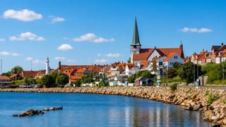 Rønne on Bornholm seen from the water, its green-spired Sankt Nicolai church rising above red-roofed houses and a small harbour lighthouse.
