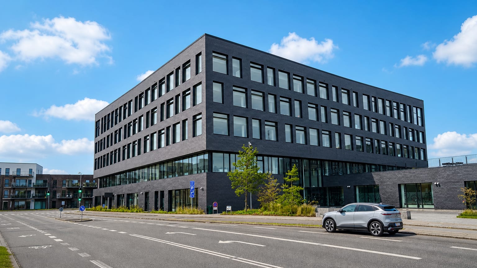 Modern dark-brick office building beside an empty street under a bright blue sky in Stenløse, Denmark