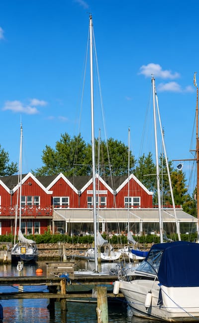 Sailboats moored in the marina in front of a red gabled clubhouse at Vallensbæk, Denmark