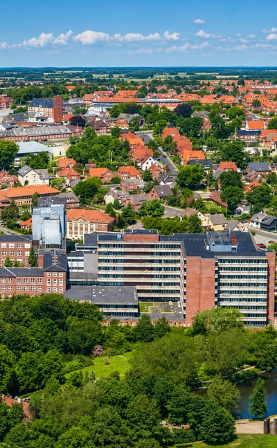 Aerial view of central Holstebro with red-brick buildings, a chimney and tiled rooftops among green parkland, Denmark