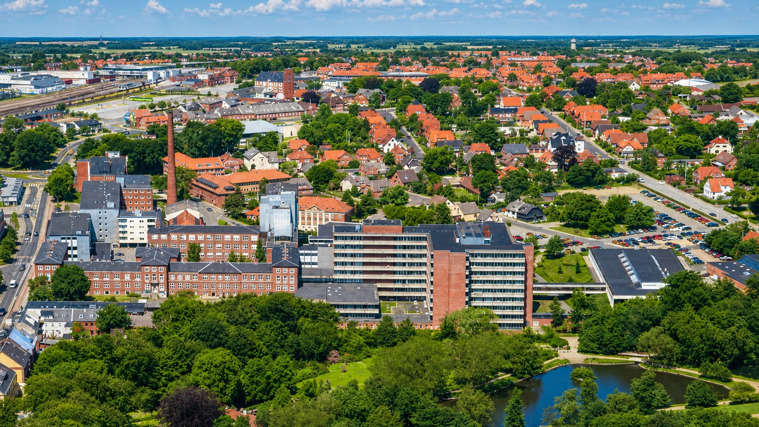 Aerial view of central Holstebro with red-brick buildings, a chimney and tiled rooftops among green parkland, Denmark