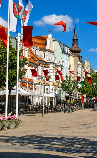 Flag-lined pedestrian shopping street with cafes and a church spire in Horsens, Denmark.
