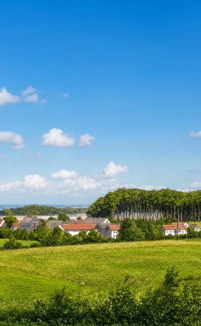 Rolling green farmland and woodland around the small Danish town of Odder, with white red-roofed houses under a blue sky.