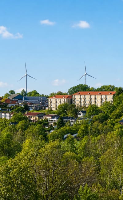 Hillside houses with red-tiled roofs and an apartment block at Skive, Denmark, with wind turbines on the horizon.