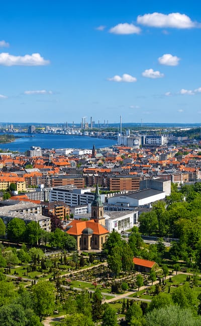 Aalborg's red-tiled old town beside the Limfjord with a green park in the foreground and industry across the water