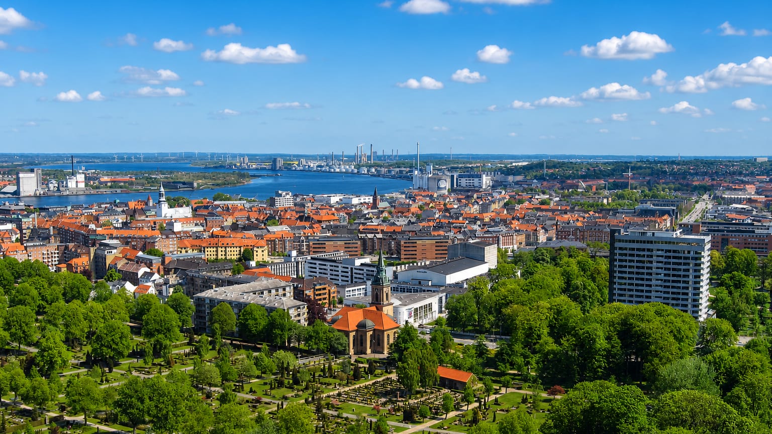 Aalborg's red-tiled old town beside the Limfjord with a green park in the foreground and industry across the water