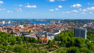 Aalborg's red-tiled old town beside the Limfjord with a green park in the foreground and industry across the water