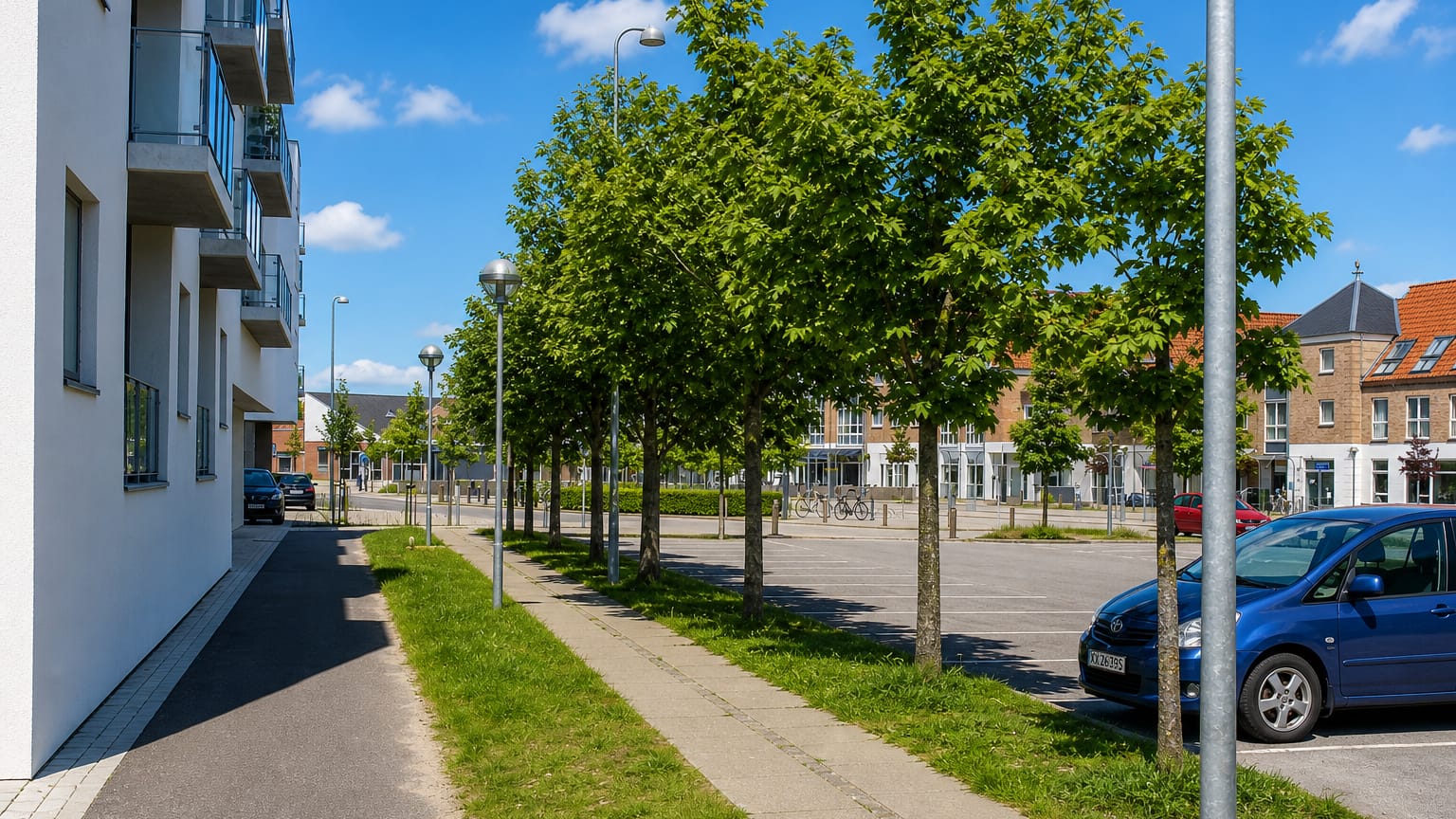 Residential street with a white apartment block, pruned trees and parked cars under blue sky in Åbybro, Denmark.