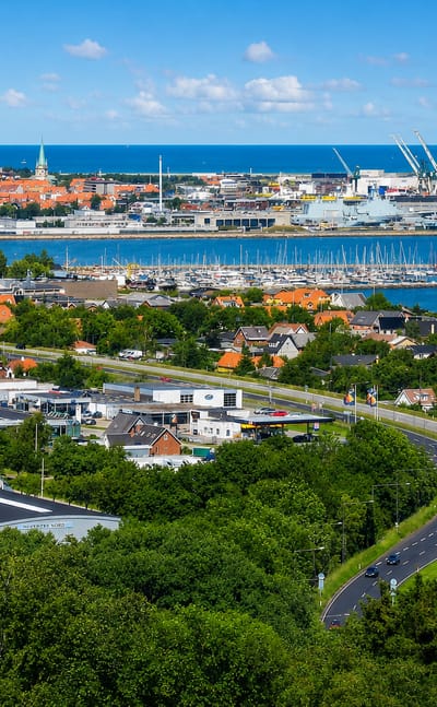 Frederikshavn's harbour and marina with port cranes, a wind turbine and the town spread along the coast
