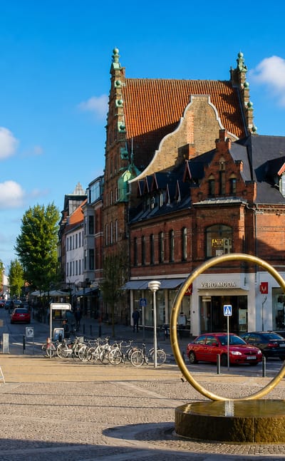 Hjorring's town square with an ornate brick building, a modern gold ring sculpture and shops, Denmark