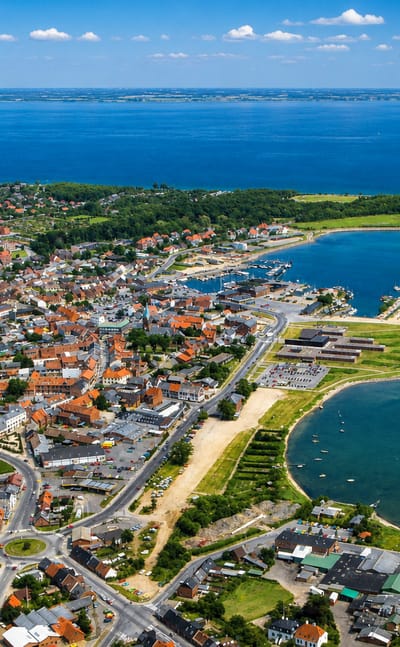 Aerial view of Nykobing Mors on the Limfjord, its red-roofed town and harbour beside a curving sandy shore.