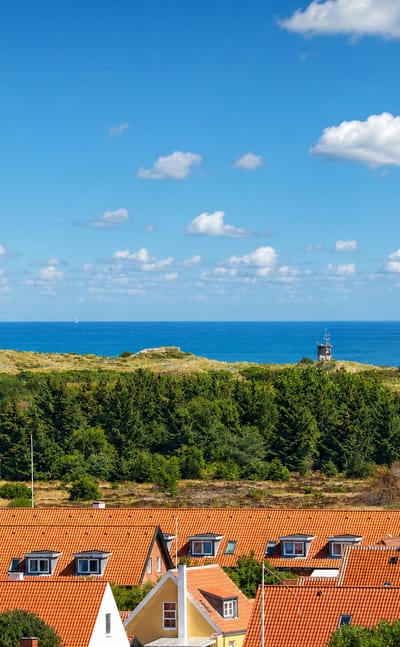 Skagen, Denmark, with its grey and white lighthouses rising over yellow houses and red rooftops by the sea.