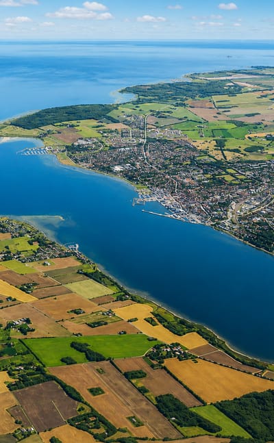 High aerial of Holbæk at the head of its fjord, surrounded by patchwork farmland and open sea