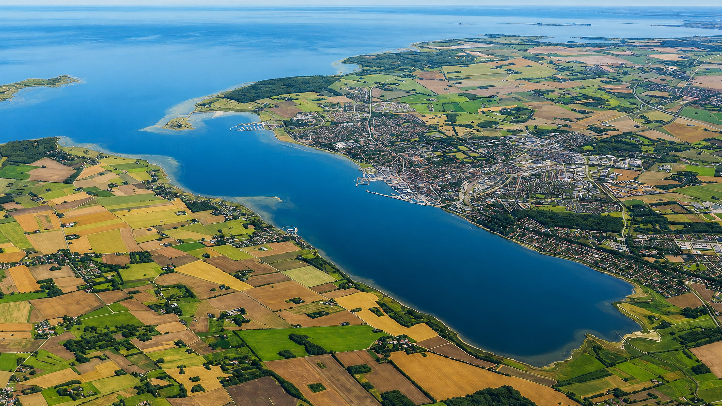 High aerial of Holbæk at the head of its fjord, surrounded by patchwork farmland and open sea