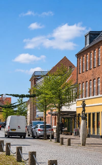 Cobbled old-town street with historic brick and yellow buildings and a bronze statue in Soro, Denmark