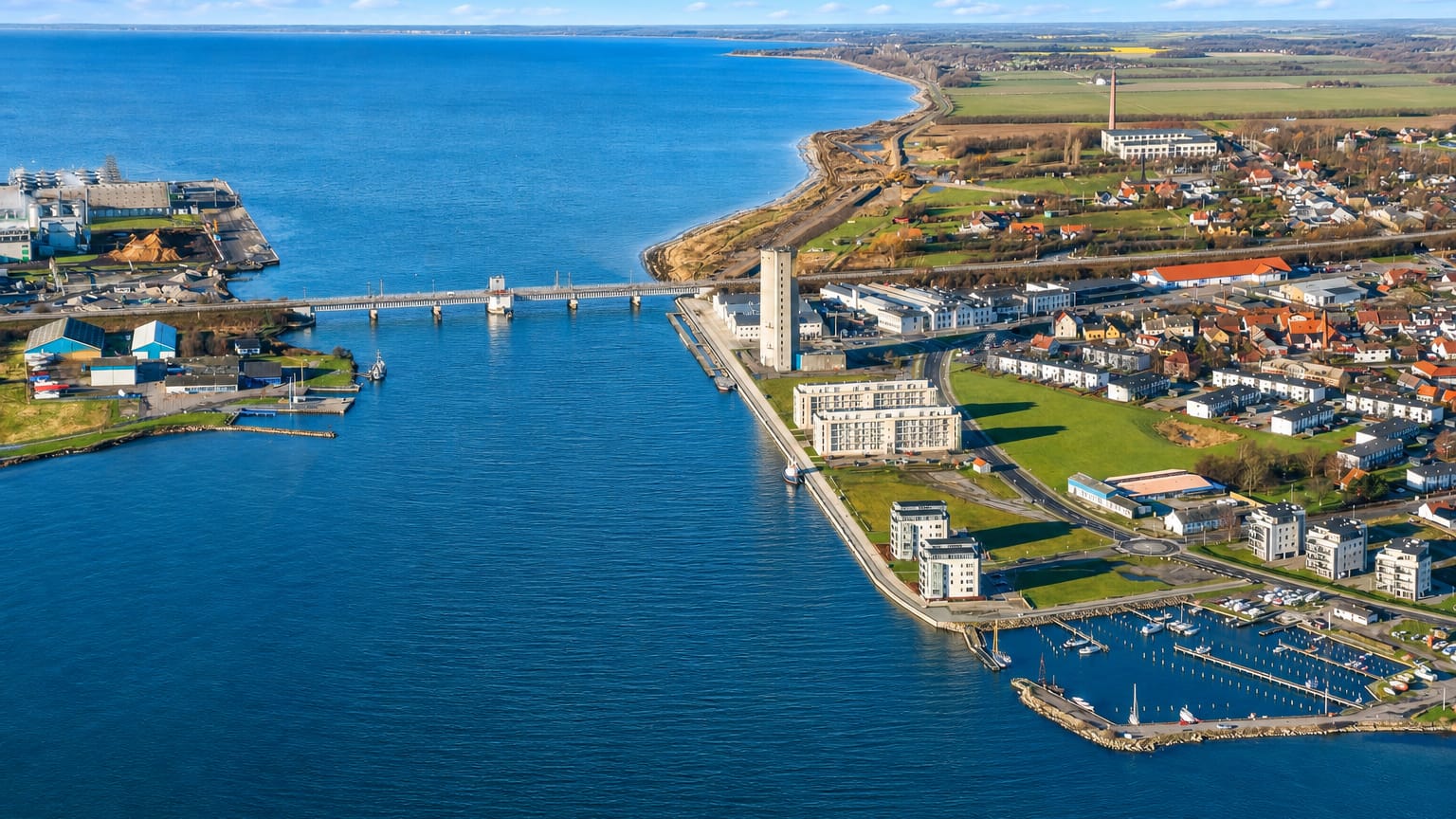 Aerial view of Vordingborg, Denmark, with a waterfront tower, marina and a bridge across the blue sound.