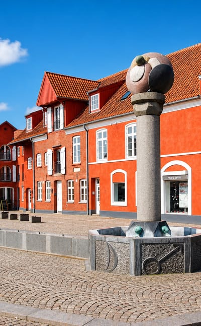 Cobbled town square with red gabled houses and a sculpture-topped fountain in Aabenraa, Denmark