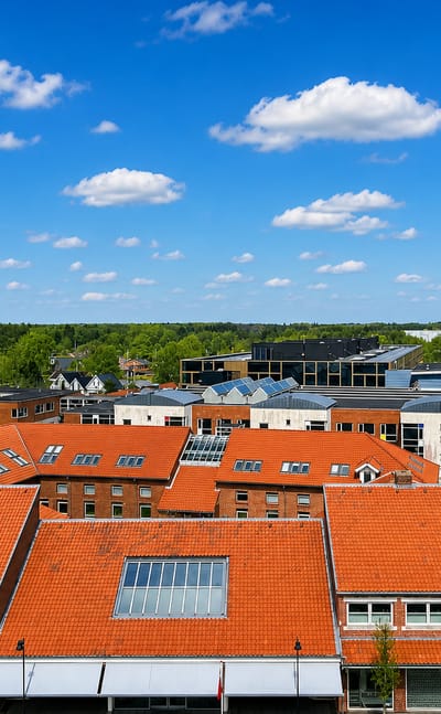 Aerial view over the red-tiled rooftops and modern buildings of Billund, Denmark, under a blue summer sky.
