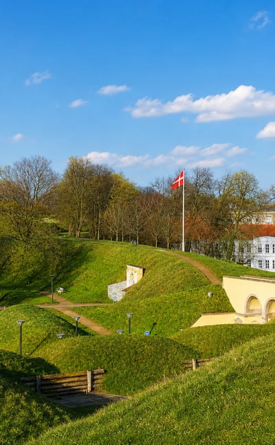 Fredericia's grassy fortress ramparts with the White Water Tower and Danish flag under blue sky