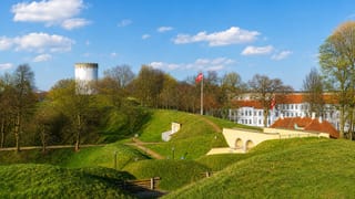 Fredericia's grassy fortress ramparts with the White Water Tower and Danish flag under blue sky