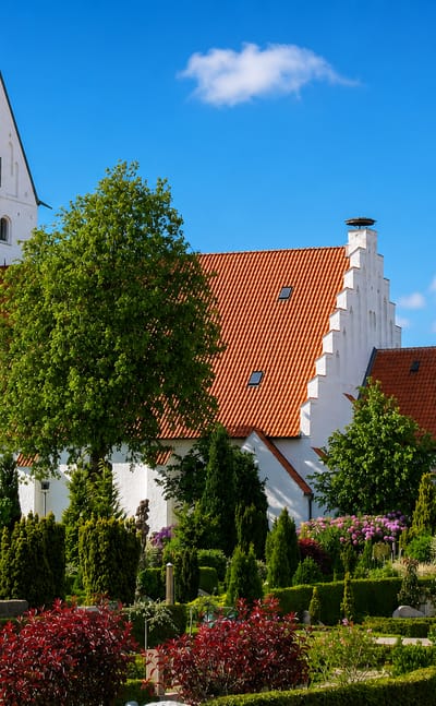 Whitewashed Grindsted church with stepped gables and a red-tiled roof above a landscaped churchyard, Denmark.
