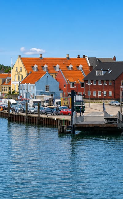 Colourful gabled houses and a moored fishing boat along Nordby's harbour and ferry berth on Fanø under a clear blue sky.