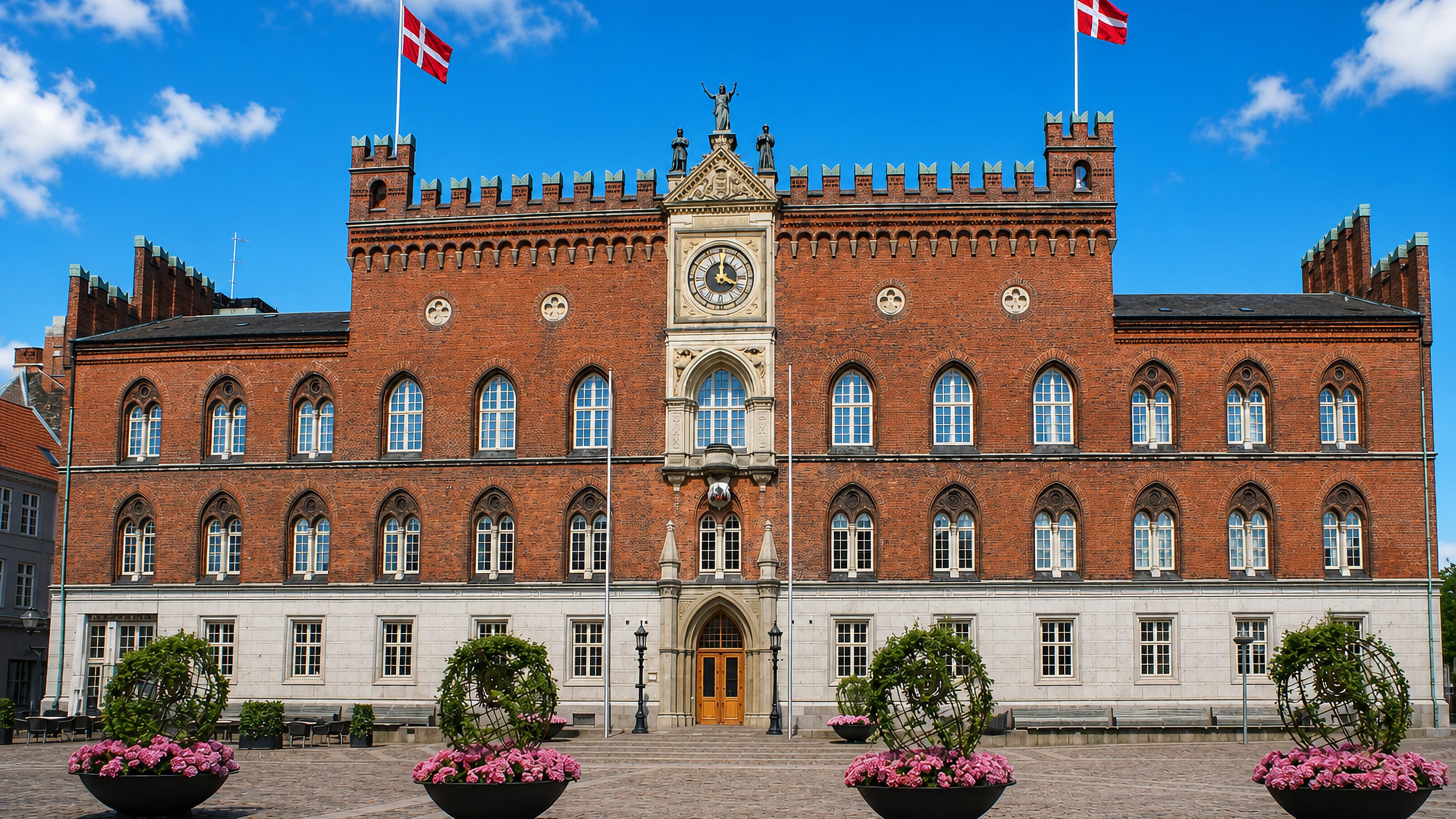 Odense City Hall's red-brick facade with clock gable and Danish flags on Flakhaven square in central Odense.