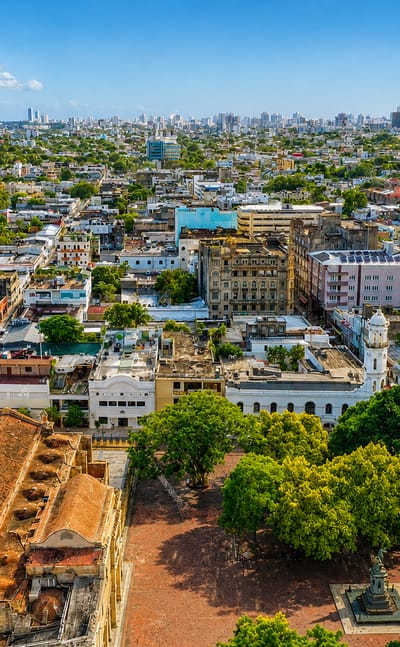 Aerial view of Santo Domingo's Colonial Zone with stone monuments and the modern skyline along the coast.