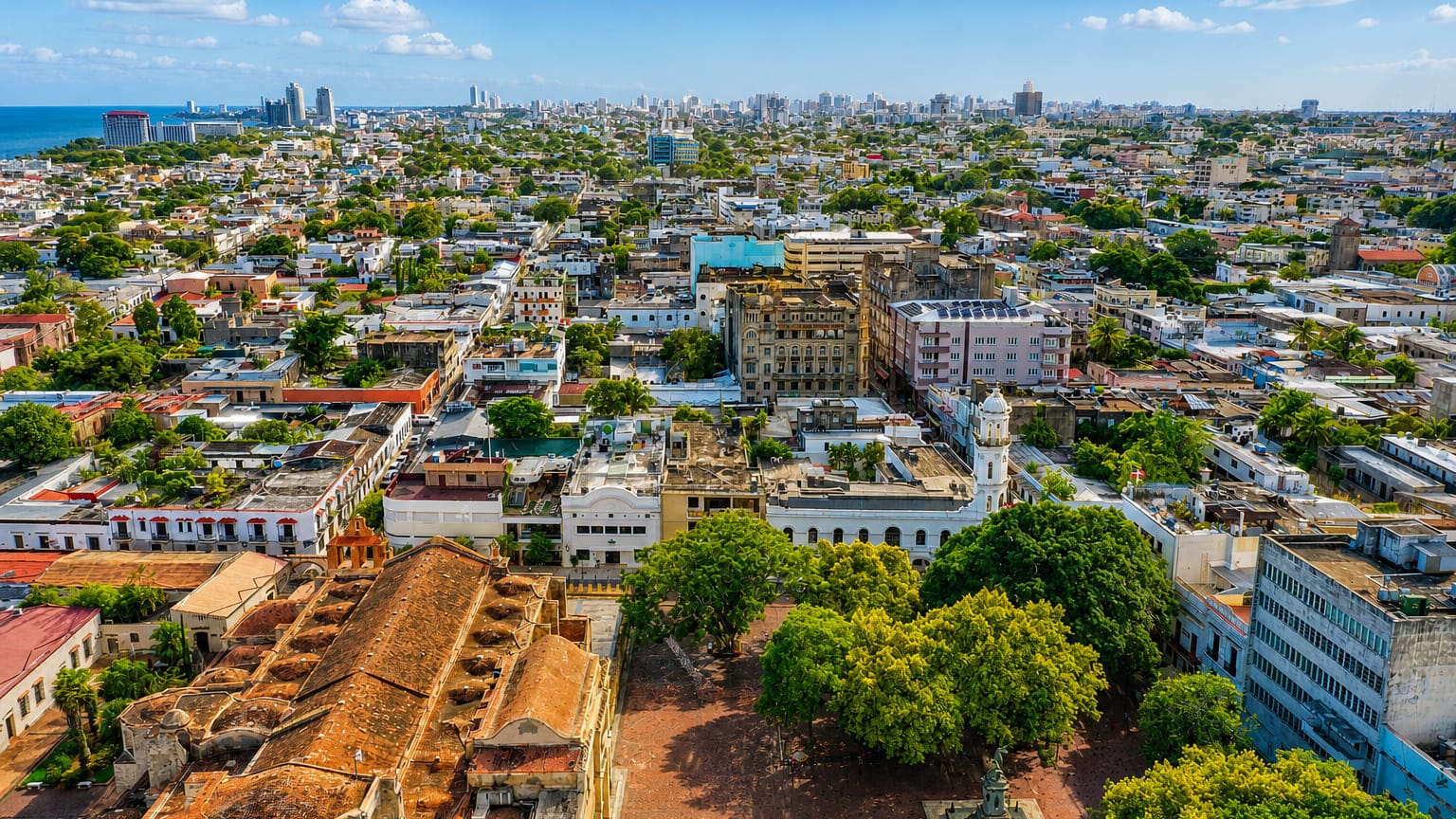 Aerial view of Santo Domingo's Colonial Zone with stone monuments and the modern skyline along the coast.