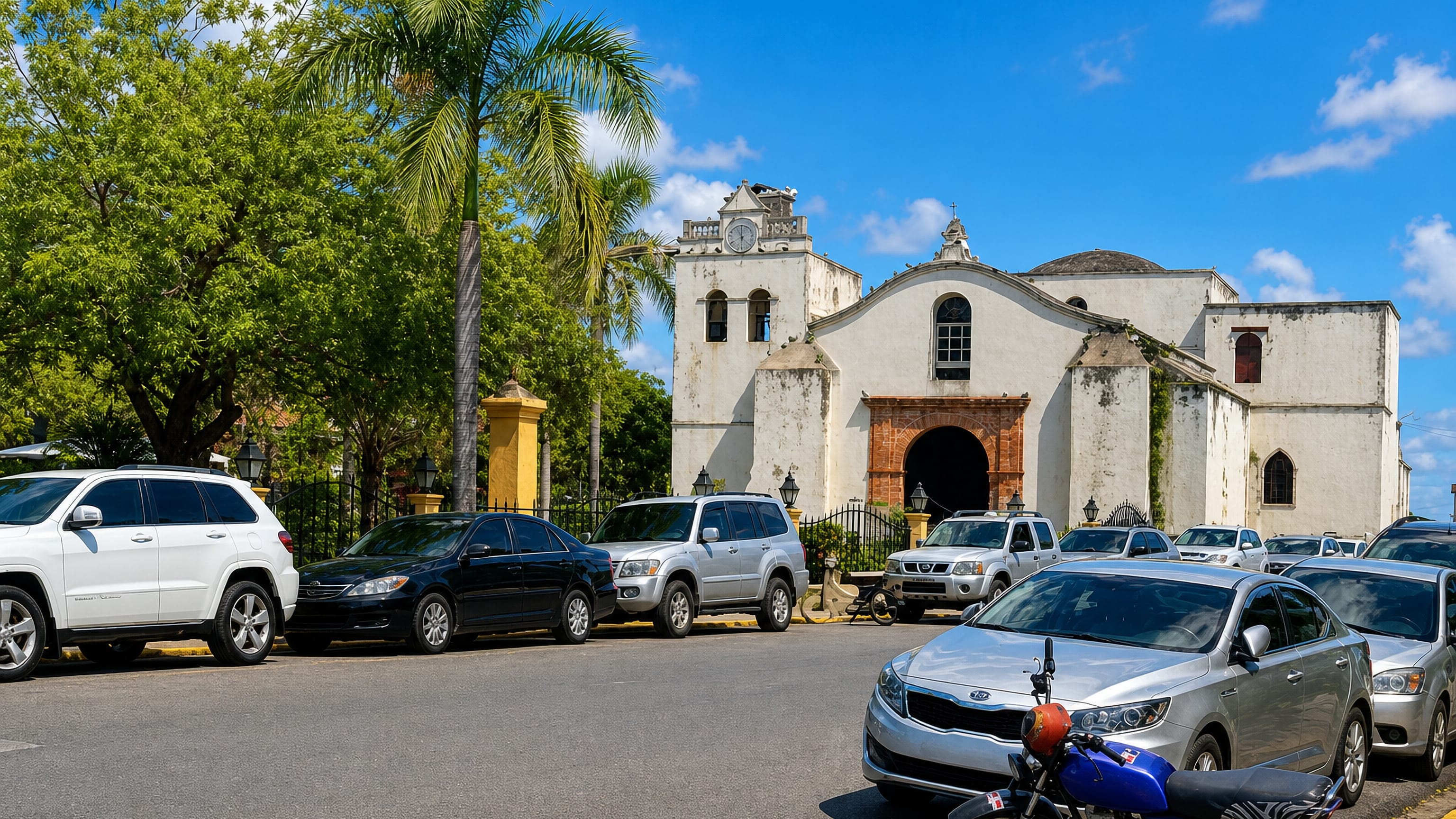 The old white colonial church of Salvaleon de Higuey, Dominican Republic, behind a row of parked cars.
