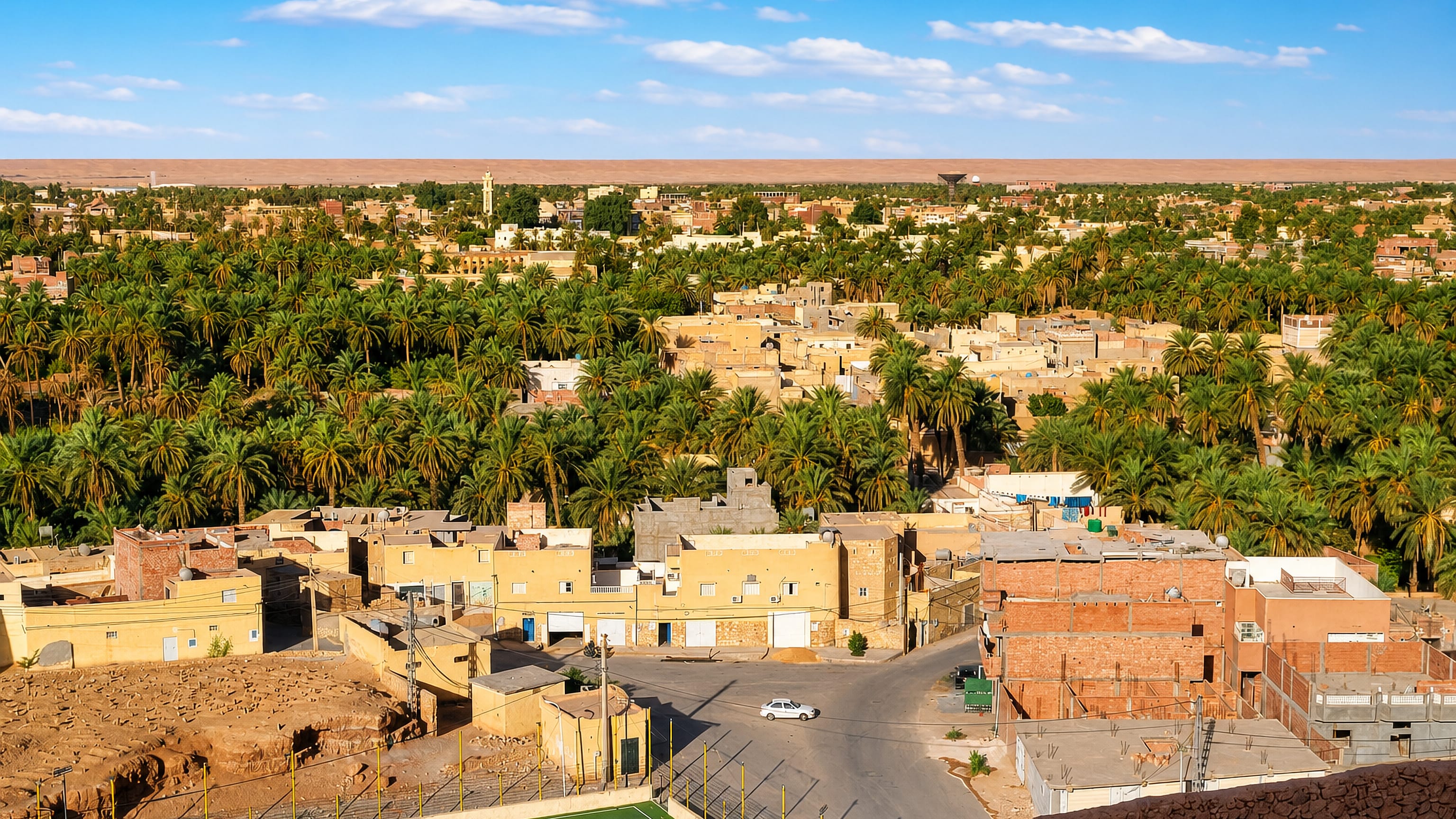Ochre houses and dense palm groves of the El Menia oasis, Algeria, with Sahara dunes on the horizon