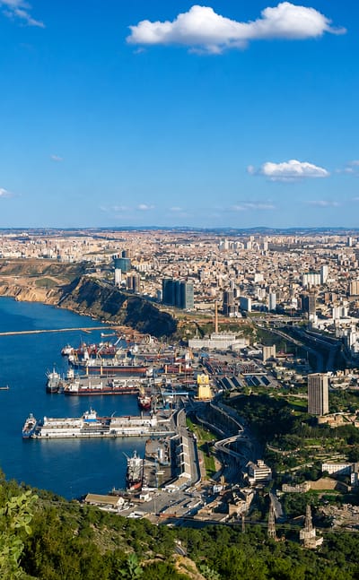 Aerial view of Oran's Mediterranean harbour, ships and hillside cityscape under a blue sky