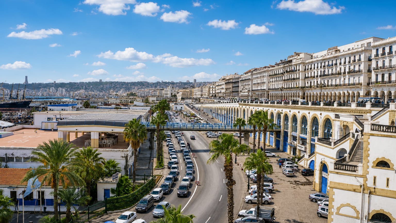 Algiers waterfront with its white arcaded boulevard buildings curving along the Bay of Algiers under a blue sky.