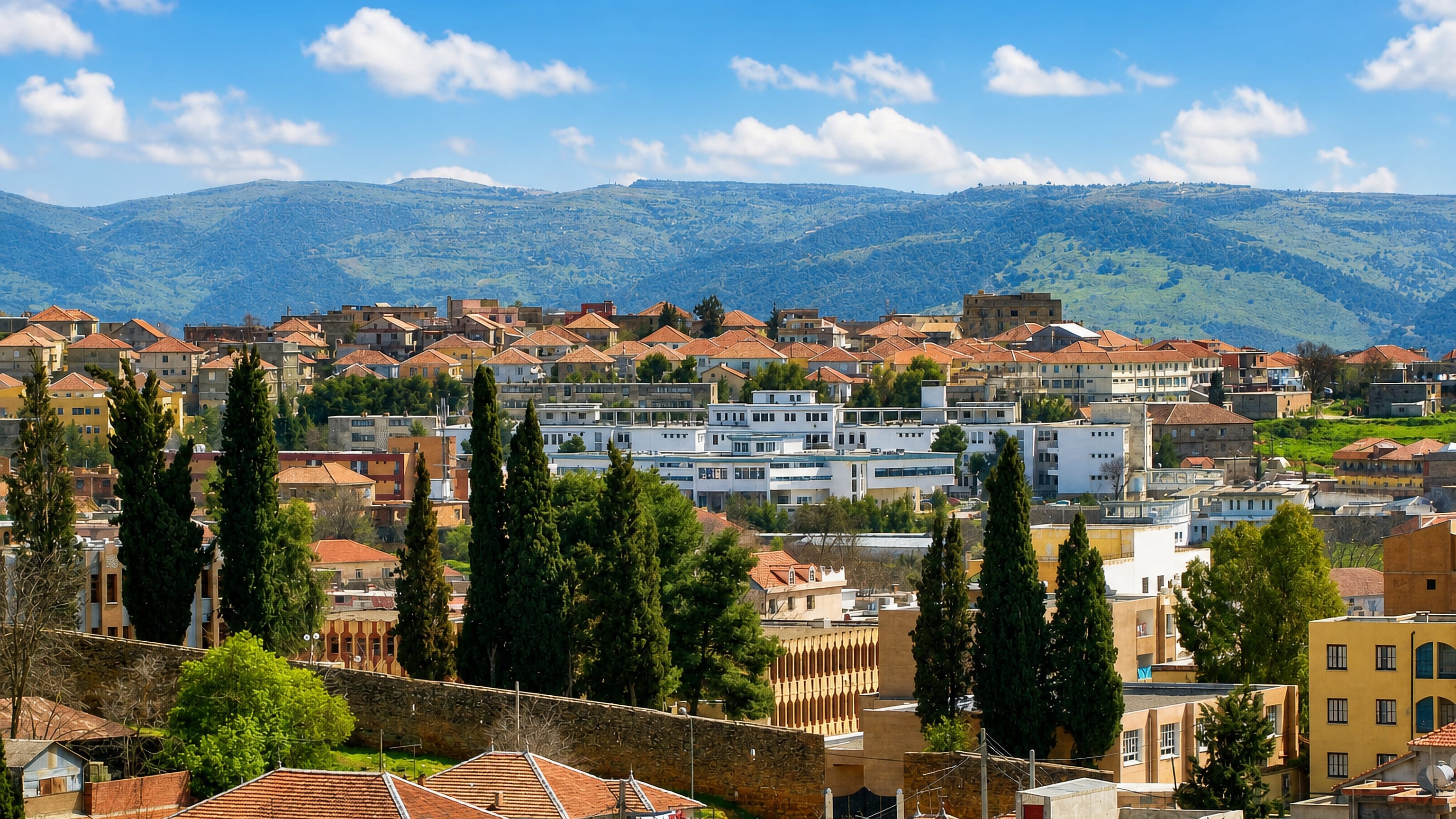 Red-tiled roofs and cypress trees of Medea rising toward the green Tell Atlas hills of northern Algeria.