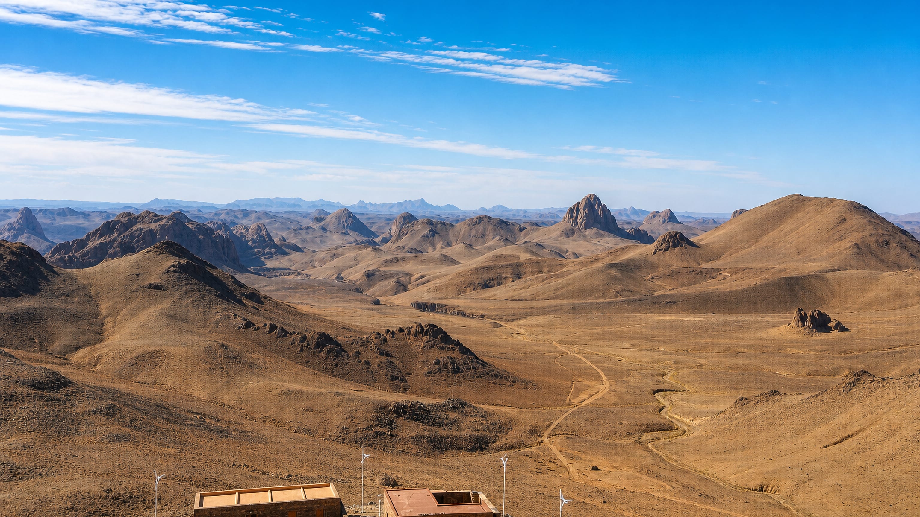 Volcanic peaks of the Hoggar massif above ochre desert near Tamanghasset, with stone shelters in the foreground